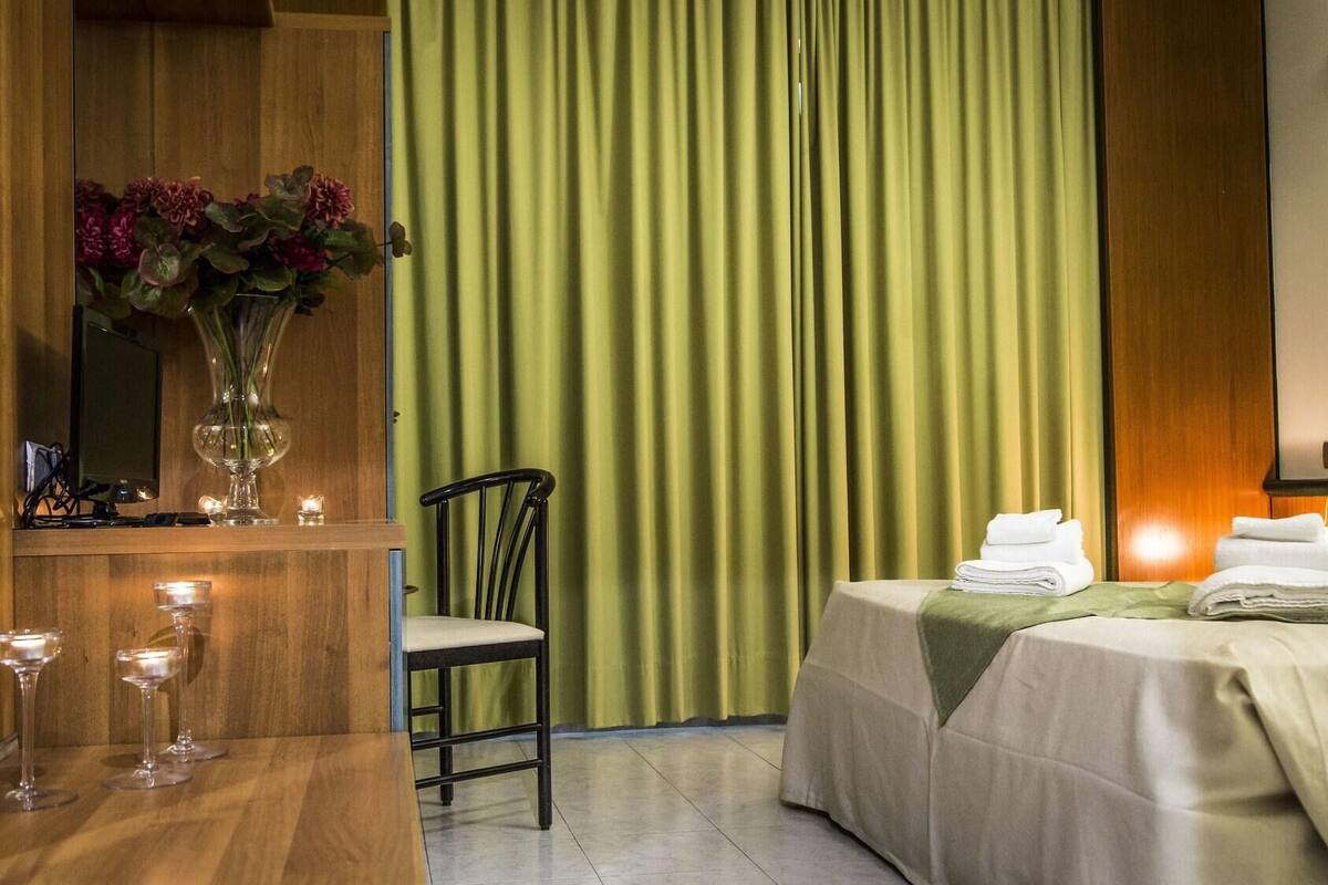 Une chambre d’hôtel avec un bureau en bois, une chaise, un lit recouvert d’une couverture verte et un miroir au mur.