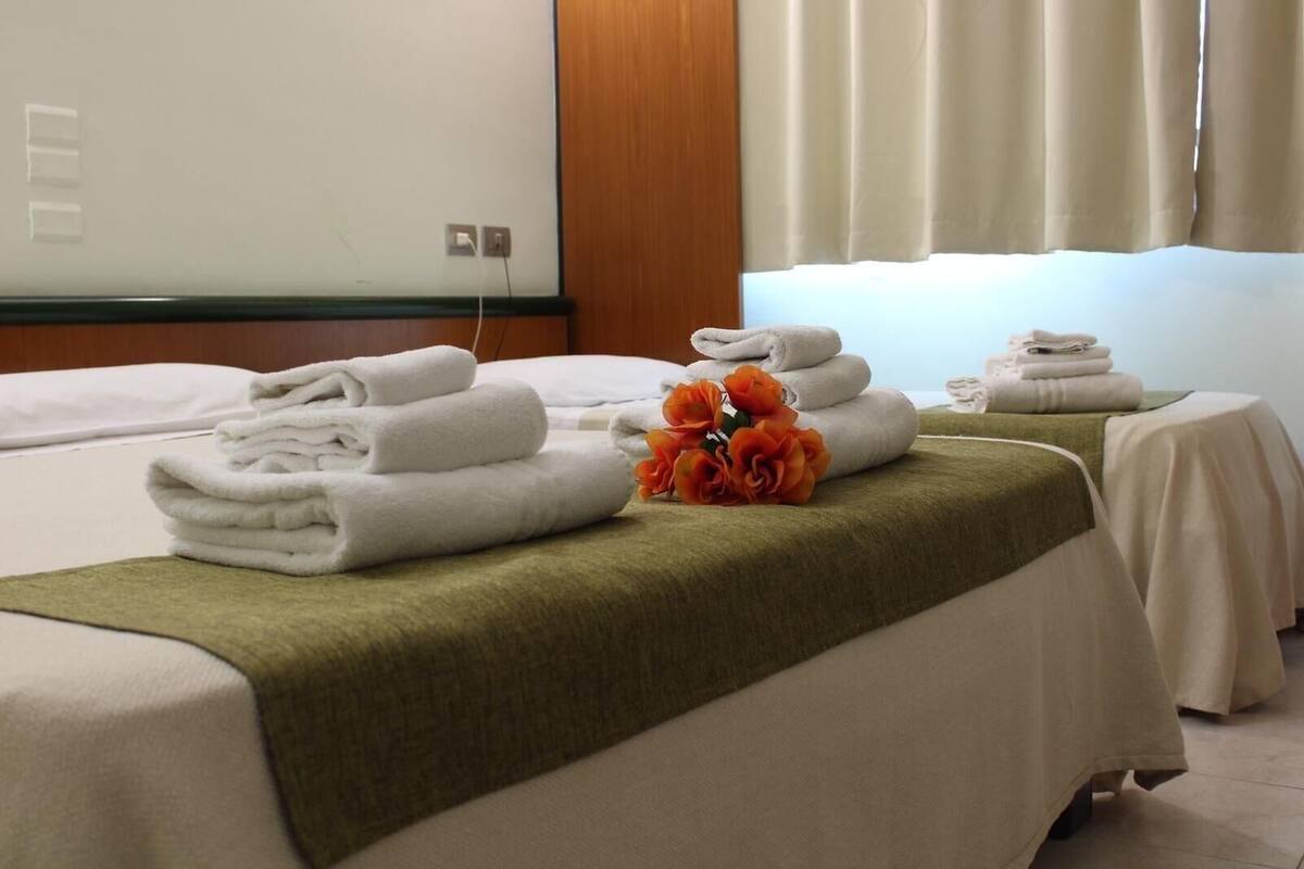 Une chambre d’hôtel avec deux lits, chacun agrémenté de serviettes blanches soigneusement pliées et d’un plaid vert. Un bouquet de fleurs oranges est placé sur le lit, entre les deux.