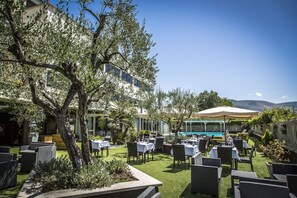 An outdoor dining area with tables and chairs, a pool, and a building in the background. - Hotel Cristallo Relais Sure Hotel Collection by Be (Tivoli)