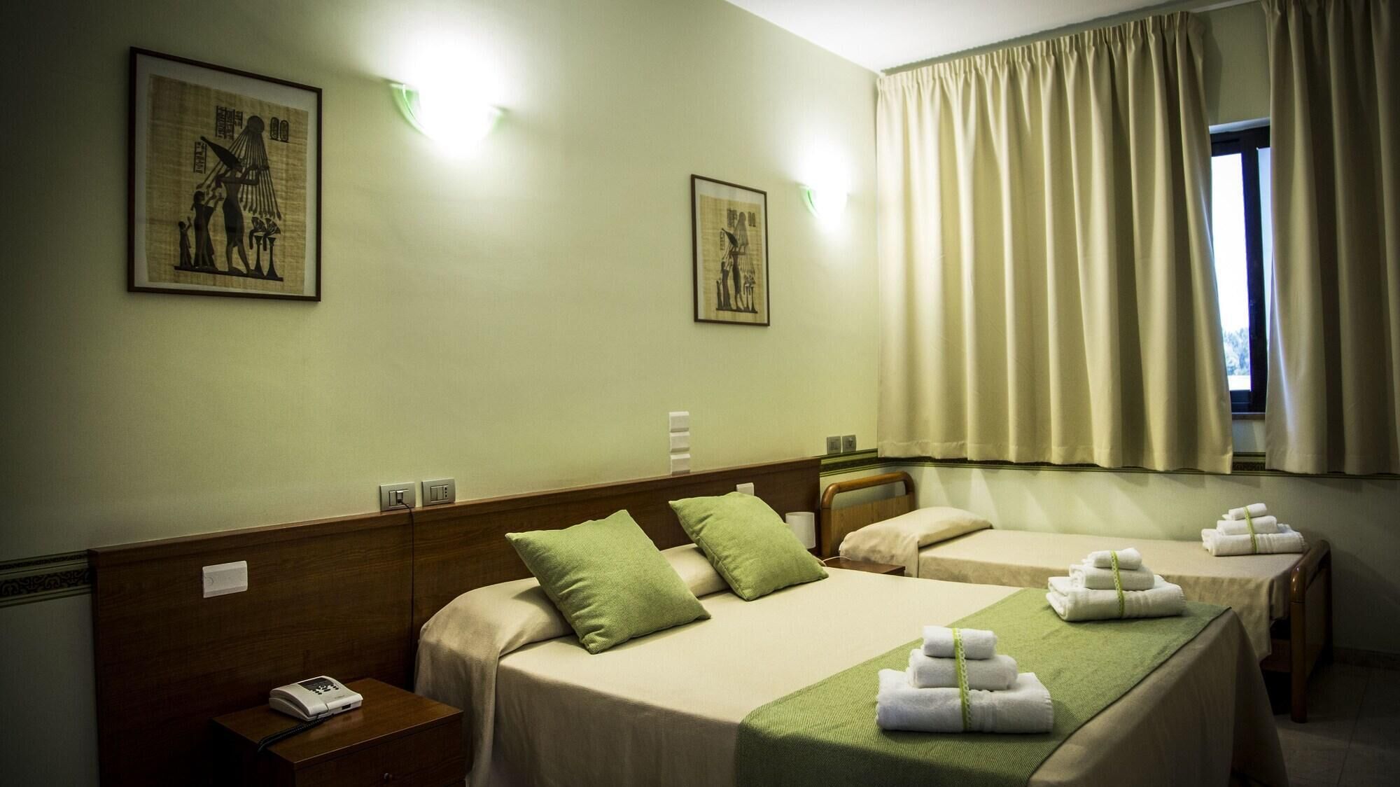 Een hotelkamer met twee bedden, een houten hoofdbord, groene kussens en een raam met gordijnen.
