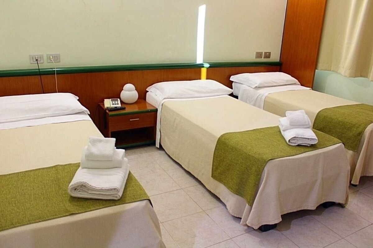 A hotel room with two single beds, a nightstand with a lamp, and a small table with a phone.