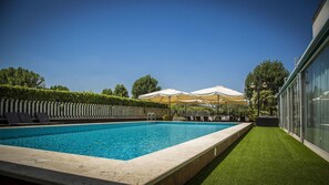 A swimming pool with a clear blue water, surrounded by a wooden deck and a green lawn. There are umbrellas and lounge chairs in the background. - Hotel Cristallo Relais Sure Hotel Collection by Be (Tivoli)