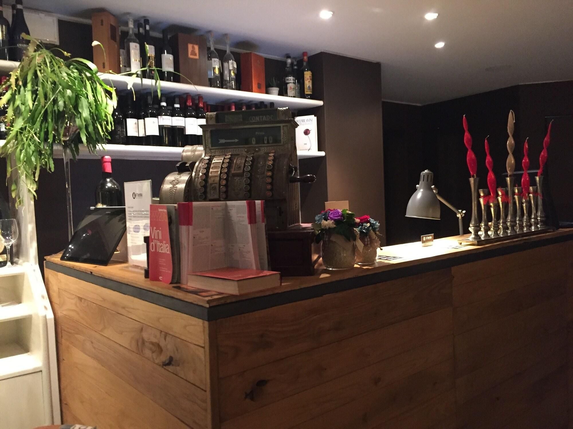 Un'area bar con un bancone in legno, bottiglie di vino, una cassa e uno scontrino.