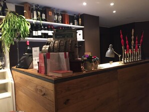 Un espace bar avec un comptoir en bois, des bouteilles de vin, une caisse enregistreuse et une autre caisse enregistreuse avec un rouleau de reçu.