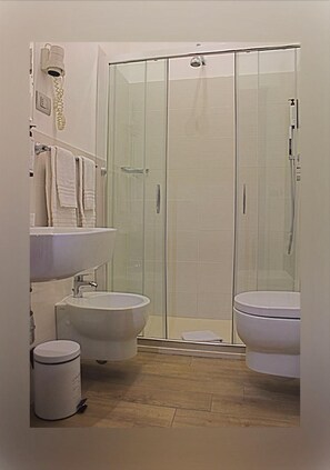 A bathroom with a glass-enclosed shower, two sinks, a toilet, and a trash can. - Hotel Cristallo Relais Sure Hotel Collection by Be (Tivoli)