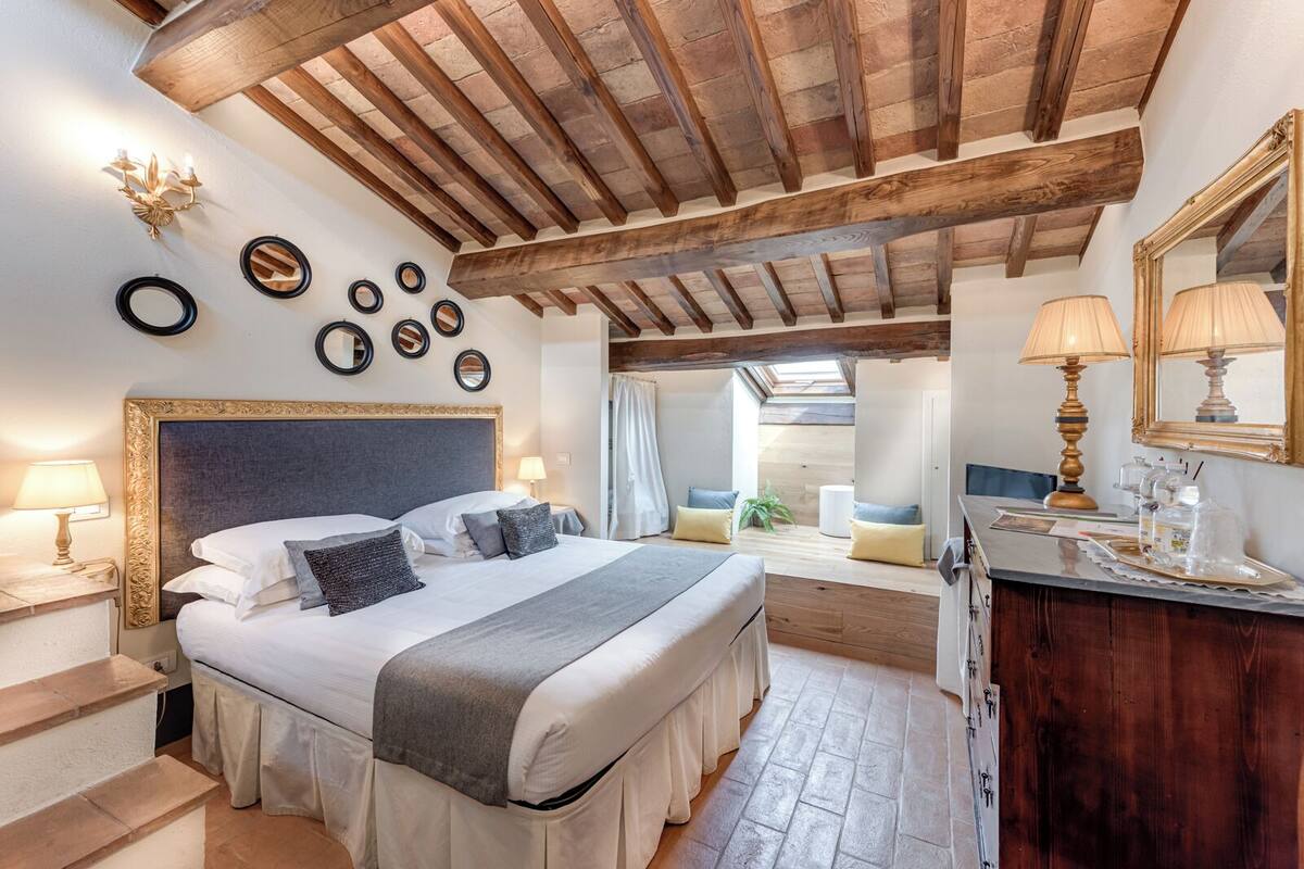 Una camera da letto con un letto grande, un soffitto in legno, una scrivania con una lampada e uno specchio.