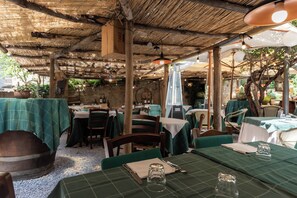 Een terrasrestaurant met tafels met groene tafelkleden, houten stoelen en hangende lampen.