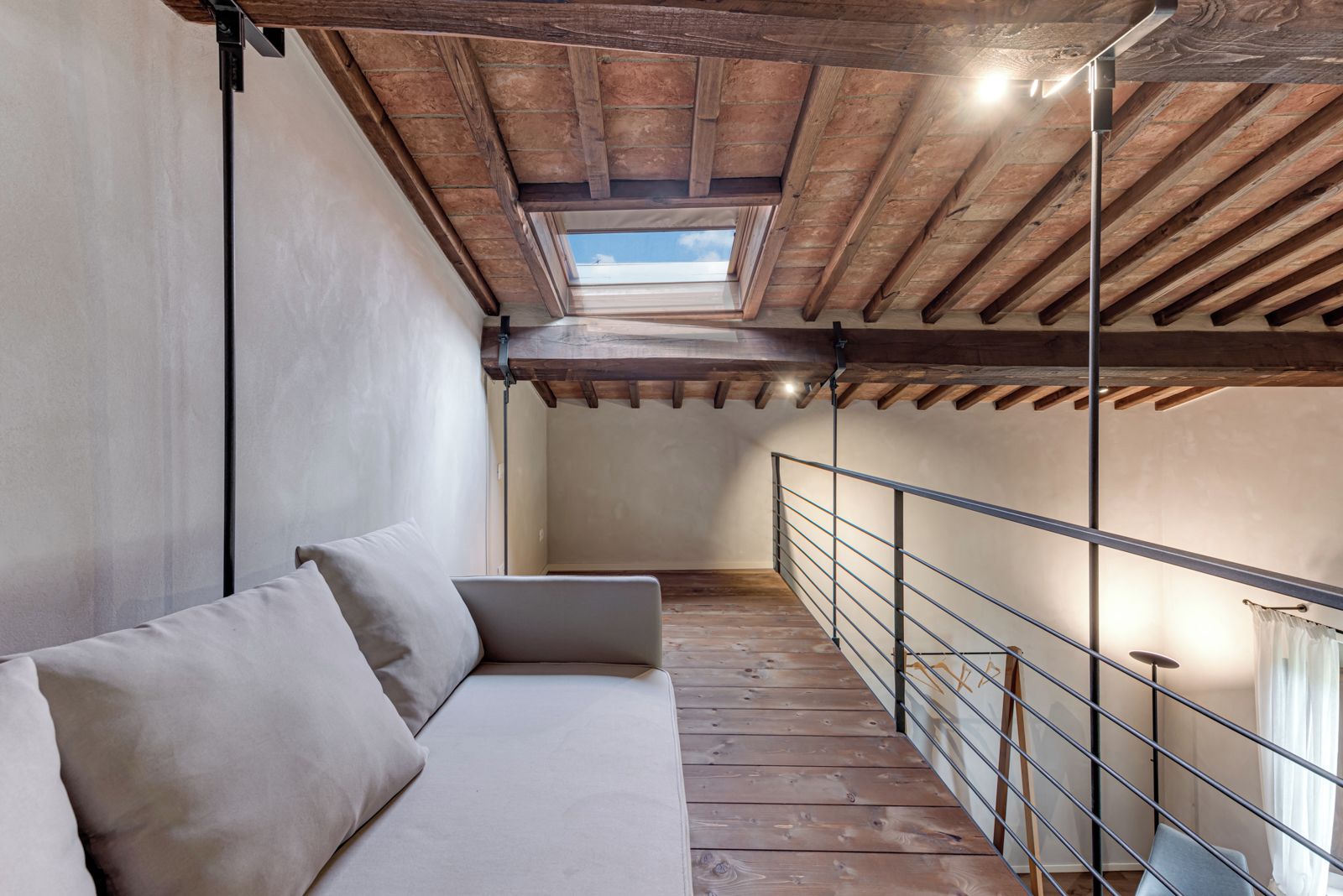 A loft-style room with a wooden ceiling, a sofa, and a metal railing.