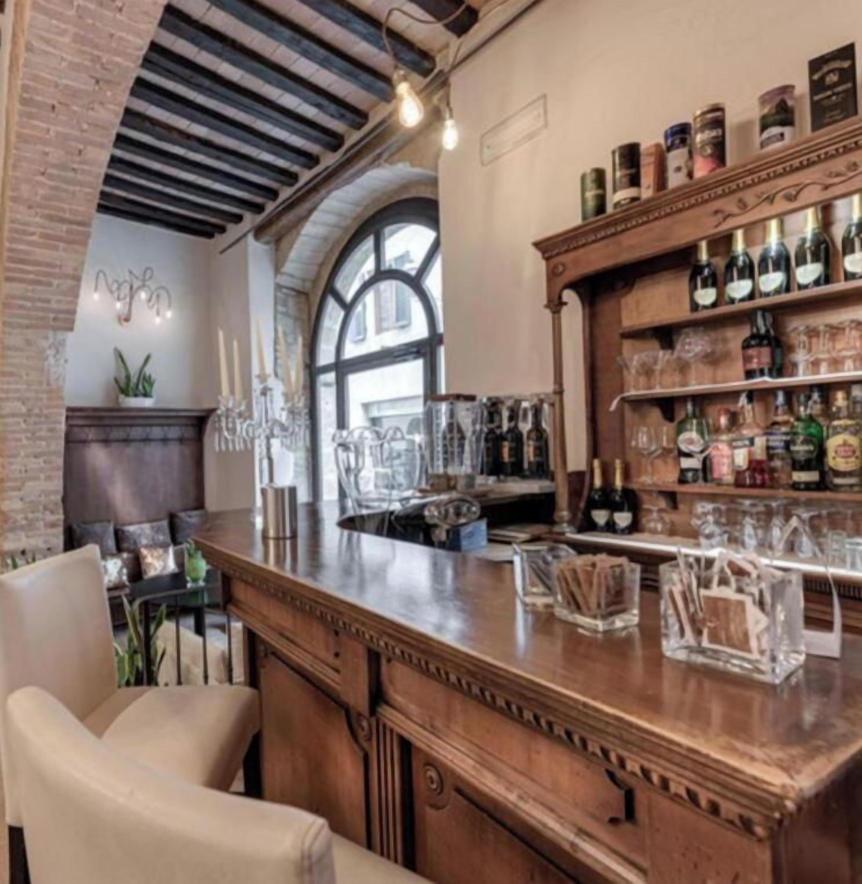 A bar area with a wooden counter, bar stools, and shelves of bottles and glasses.
