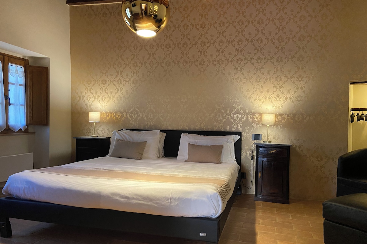 Quarto com cama grande, duas mesas de cabeceira, um espelho e um lustre.