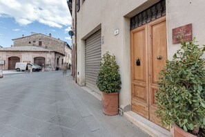 A narrow street with a closed wooden door, a potted plant, and a parked van. - B&B Borgo Medievale San Quirico D'orcia (San Quirico d'Orcia)