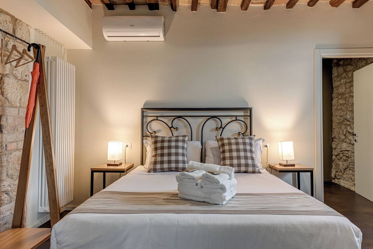 Una camera d'albergo con un letto, due comodini, una testiera e un condizionatore d'aria.