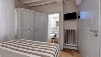 A bedroom with a bed, a TV, a radiator, and a bathroom visible through an open door.