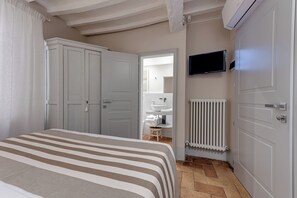 Ein Schlafzimmer mit Bett, Fernseher, Heizkörper und einem durchgehenden Türspalt sichtbaren Badezimmer.