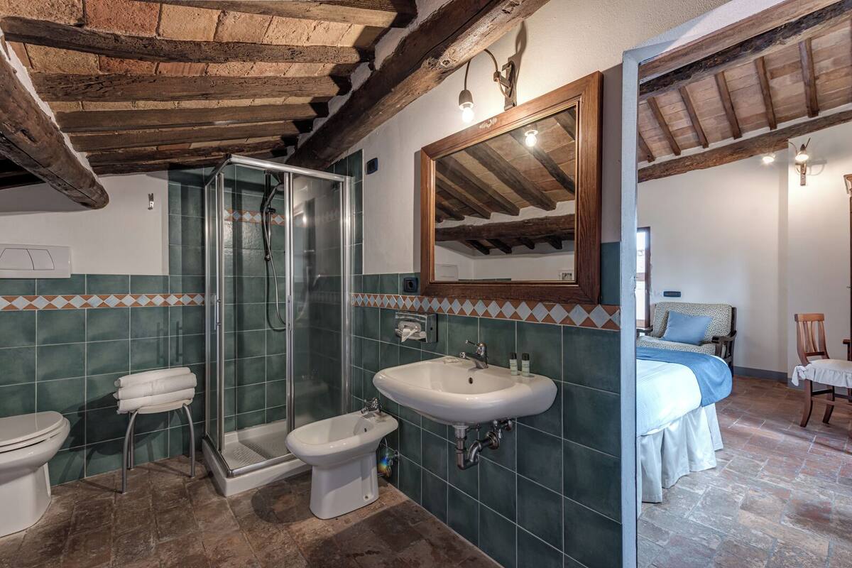 Un bagno con doccia, WC e lavandino, con travi a vista in legno e pareti piastrellate.