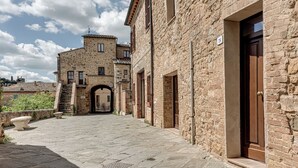 Um edifício de pedra com um arco central, uma escadaria que leva a um andar superior e uma porta à direita.