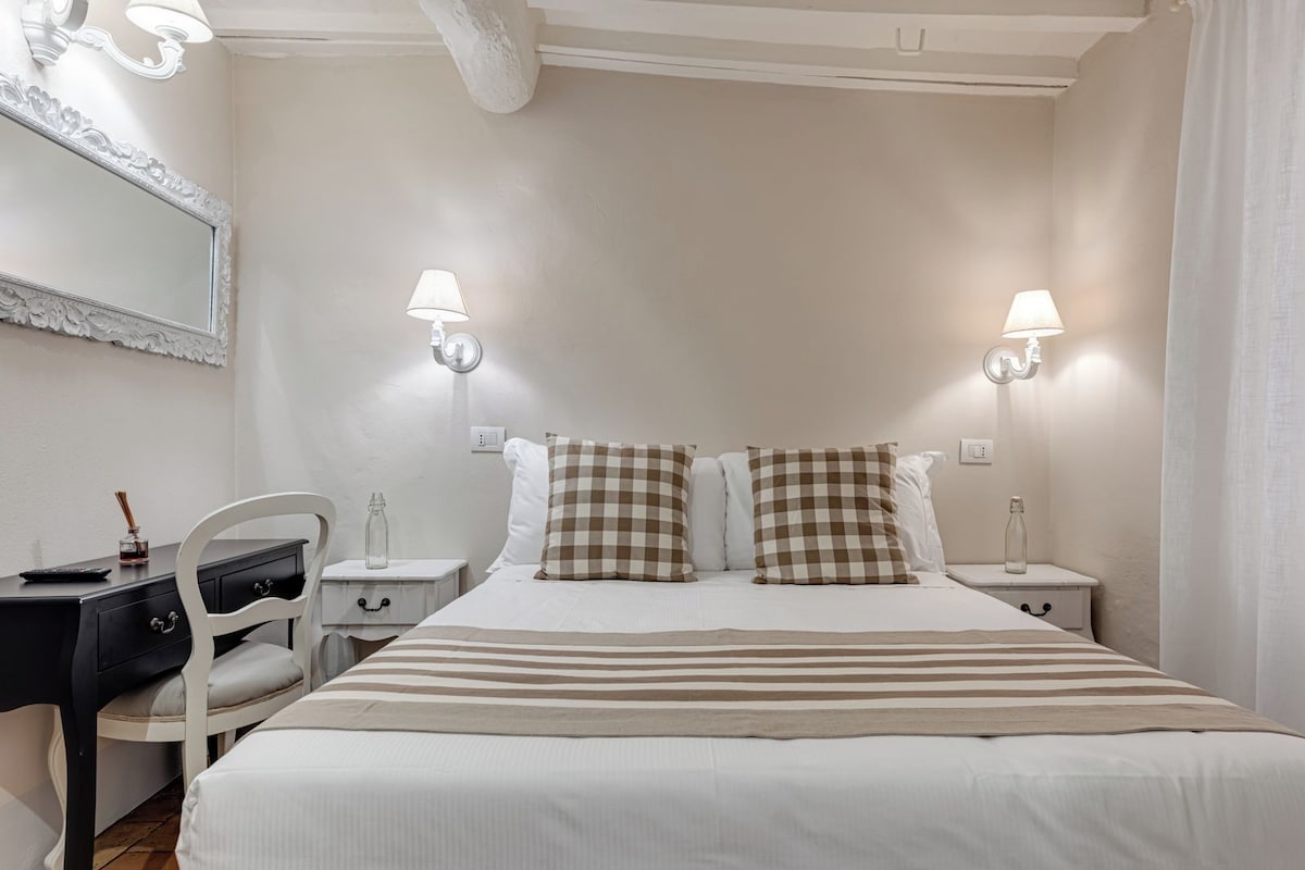 Quarto de hotel com uma cama grande, duas luminárias de cabeceira, uma escrivaninha com cadeira e um espelho na parede.