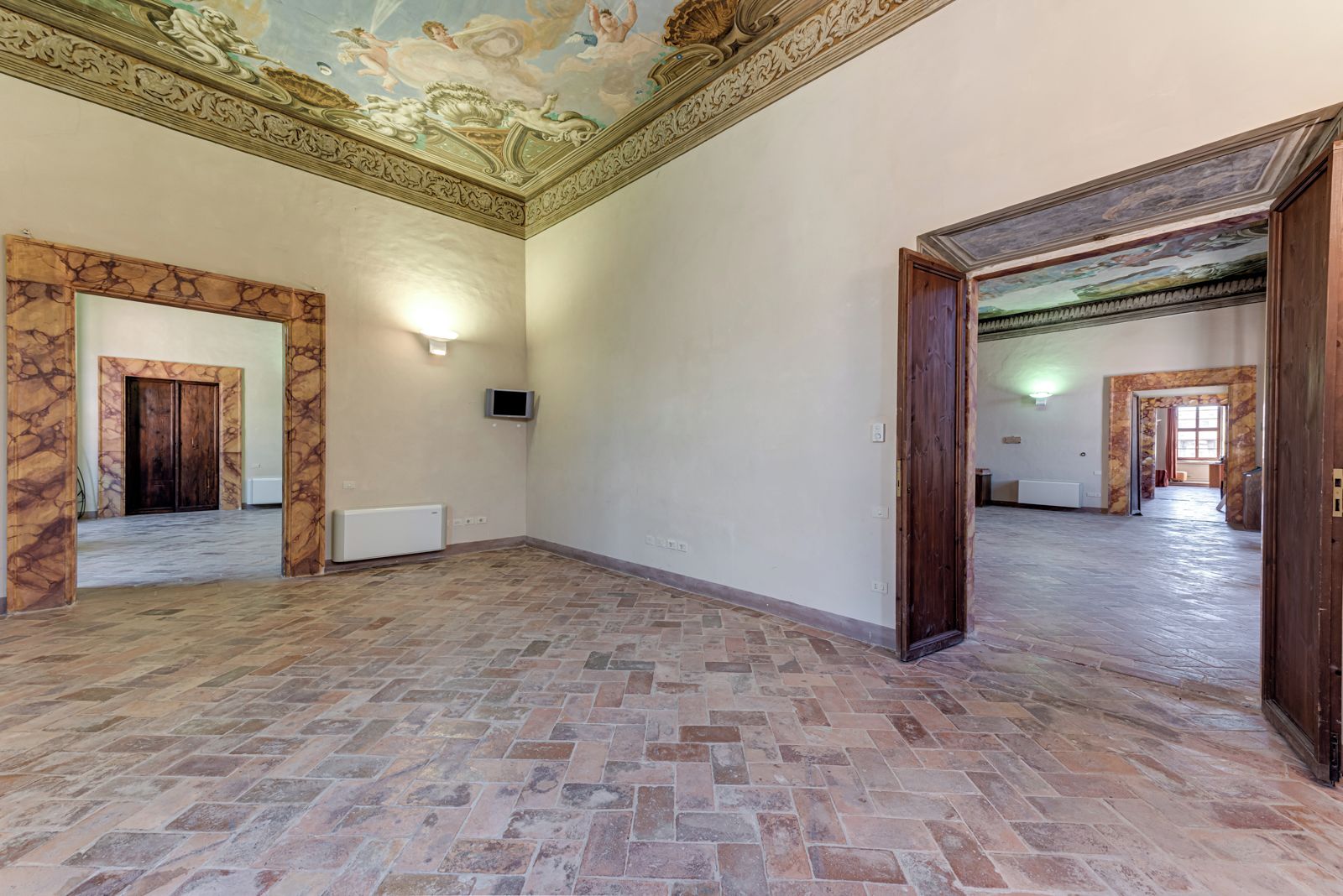 Um quarto espaçoso com piso de azulejos, porta de madeira e teto com decoração detalhada.