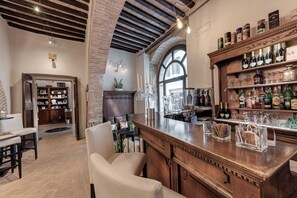 Zona bar con un bancone in legno, scaffali pieni di bottiglie di liquori e una zona con panche e sedie.