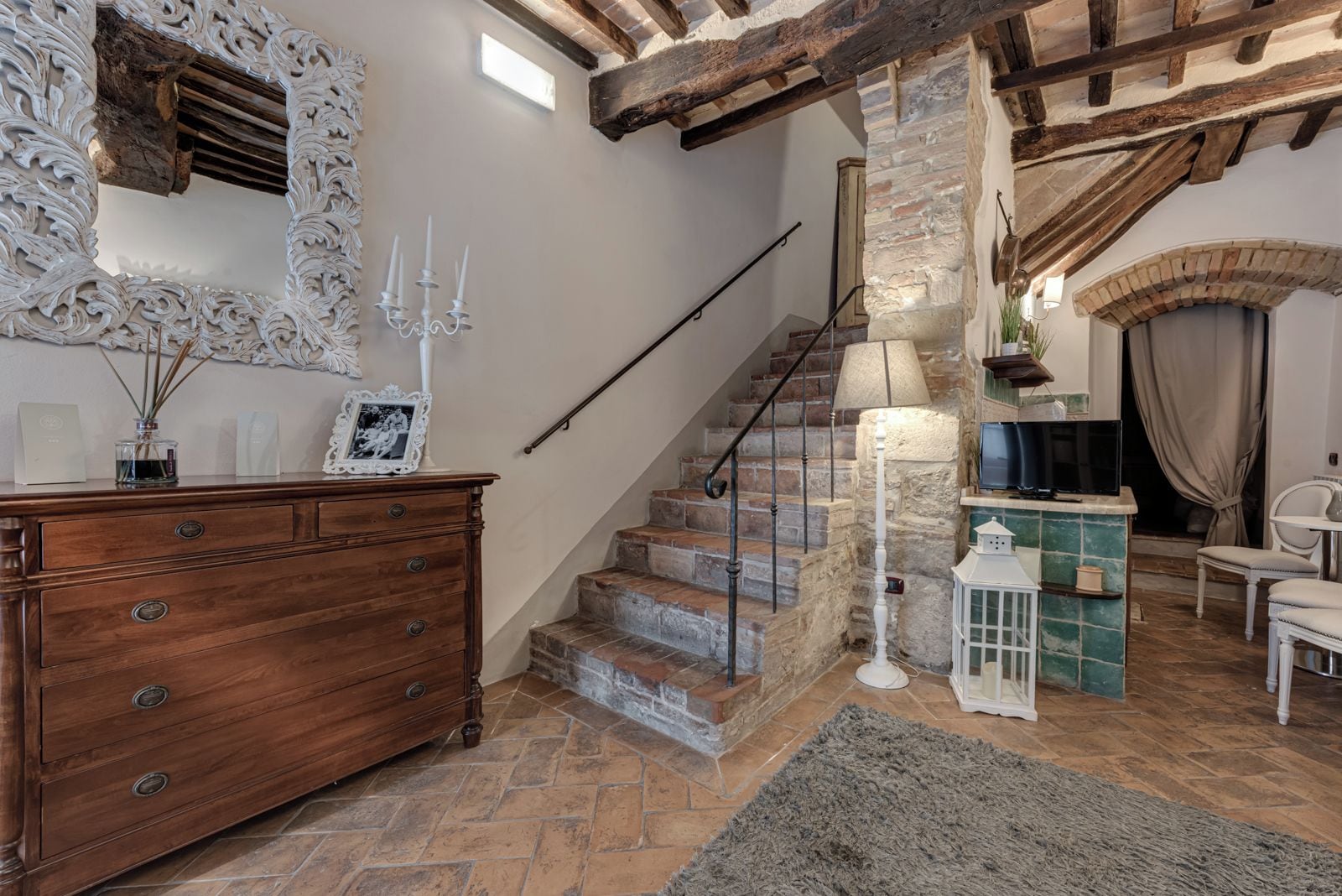 A staircase with stone steps and a wooden railing, leading to a room with a fireplace, a television, and a white chair.