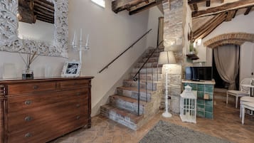 A staircase with stone steps and a wooden railing, leading to a room with a fireplace, a television, and a white chair.
