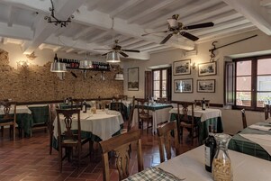 Un restaurante con mesas y sillas de madera, una pared de ladrillo con botellas de vino y ventiladores de techo.