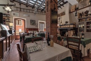 A restaurant with brick walls, wooden beams, and a variety of wine bottles on shelves. Tables are set with wine glasses and plates.