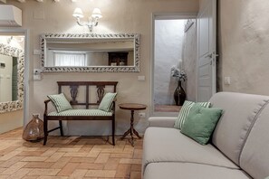 Un soggiorno con un divano, una panca di legno con cuscini a righe, un tavolino rotondo e un grande specchio con cornice decorata.