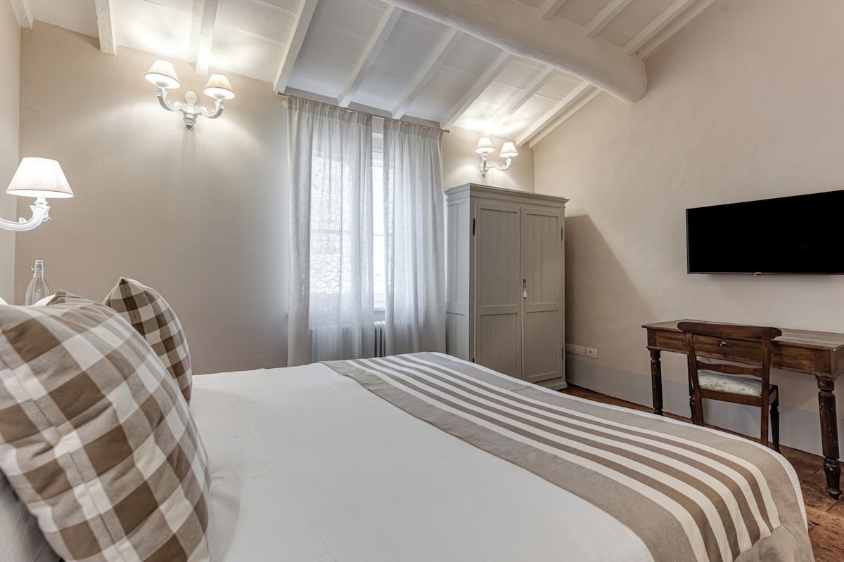 Quarto de hotel com cama, guarda-roupa, escrivaninha e televisão.
