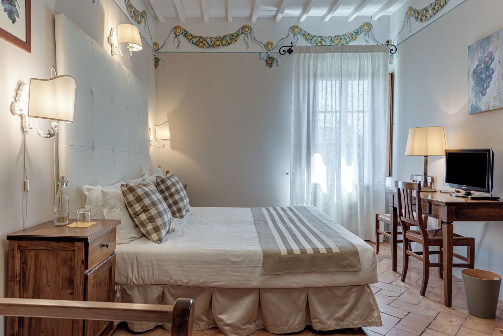 A bedroom with a bed, bedside tables, a desk with a chair, a television, and a window with curtains.