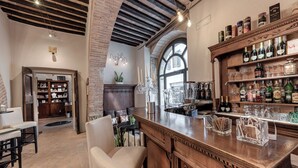A bar area with a wooden counter, shelves of liquor bottles, and a seating area with a bench and chairs. - B&B Borgo Medievale San Quirico D'orcia (San Quirico d'Orcia)