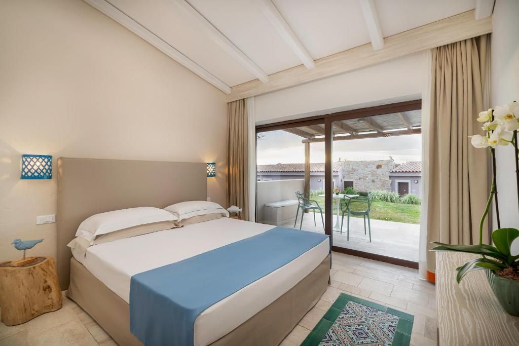 A bedroom with a bed, a nightstand, a lamp, a window with curtains, and a view of the outside.