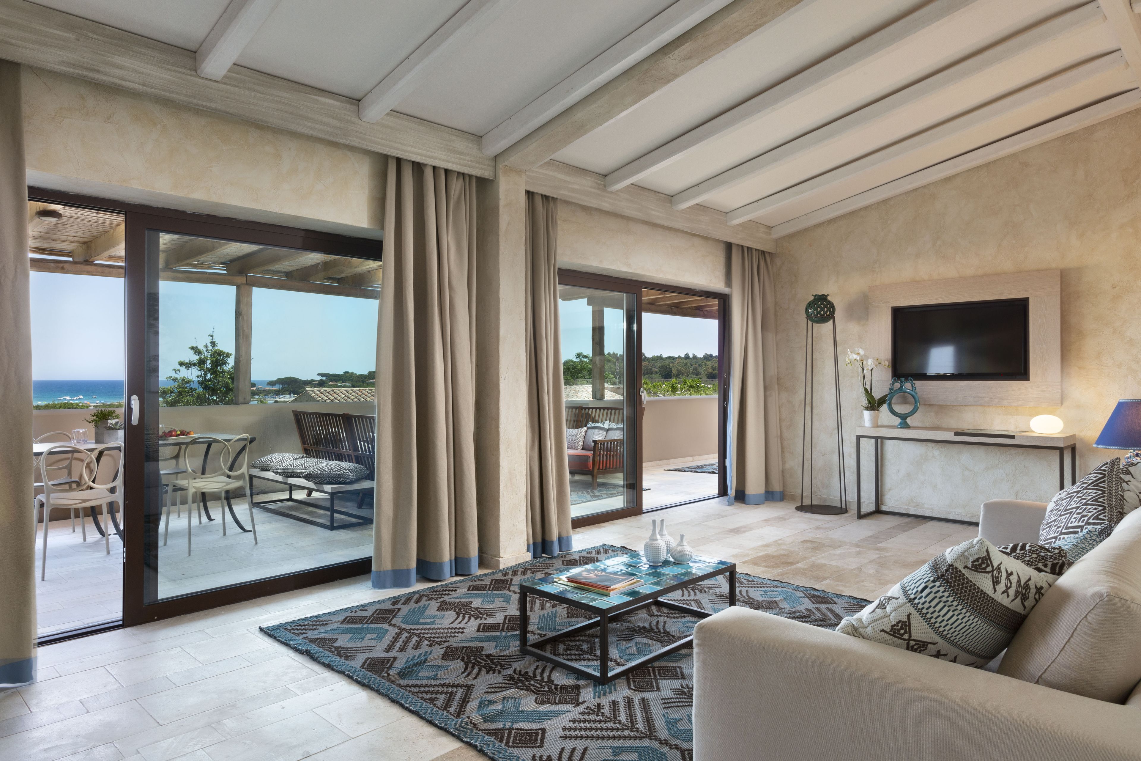 A spacious living area with a large sliding glass door leading to an outdoor patio, a comfortable sofa, a coffee table, and a flat-screen TV mounted on the wall.