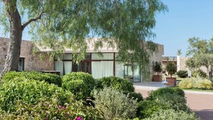 Un bâtiment moderne aux murs en pierre et aux grandes fenêtres, entouré de jardins et d’arbres bien entretenus.
