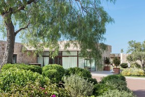 A modern building with stone walls and large windows, surrounded by well-maintained gardens and trees. - Baglioni Resort Sardinia (San Teodoro)