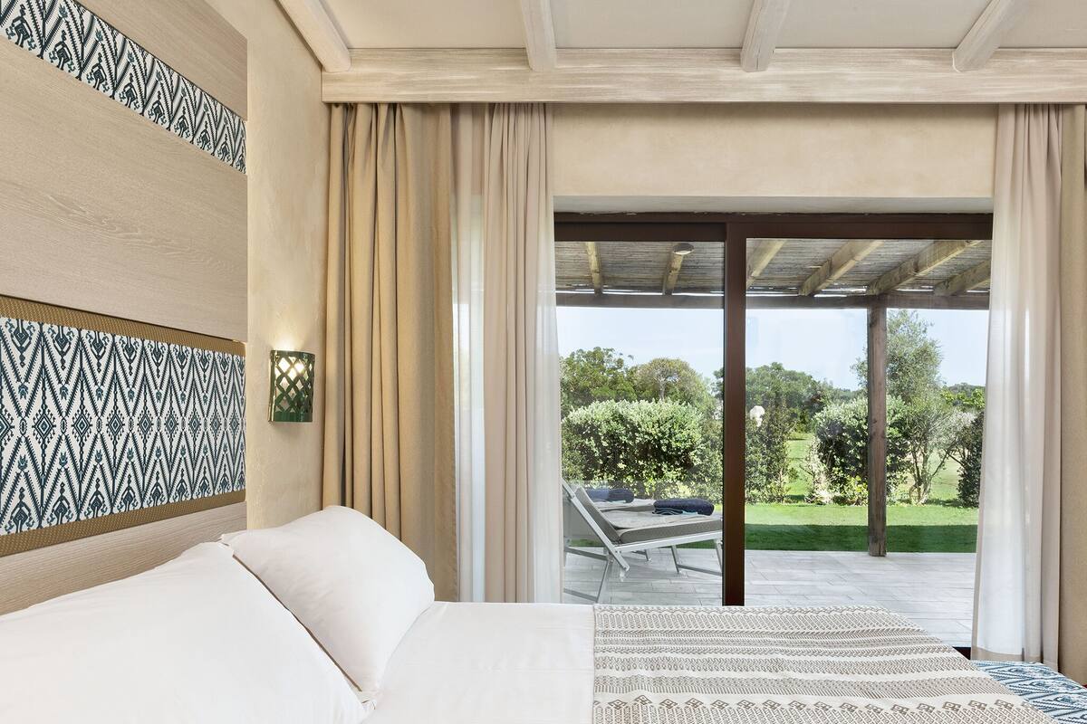 Une chambre à coucher avec un lit, un mur décoré d’un motif, une fenêtre avec des rideaux et une vue sur l’extérieur.
