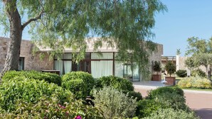 Un edificio moderno con muros de piedra y ventanas amplias, rodeado de jardines cuidados y árboles.