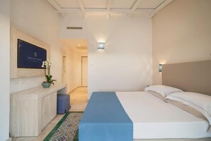 Ein Hotelzimmer mit Bett, einem an der Wand befestigten Fernseher, einem kleinen Tisch mit Pflanze und einer blauen Tagesdecke.