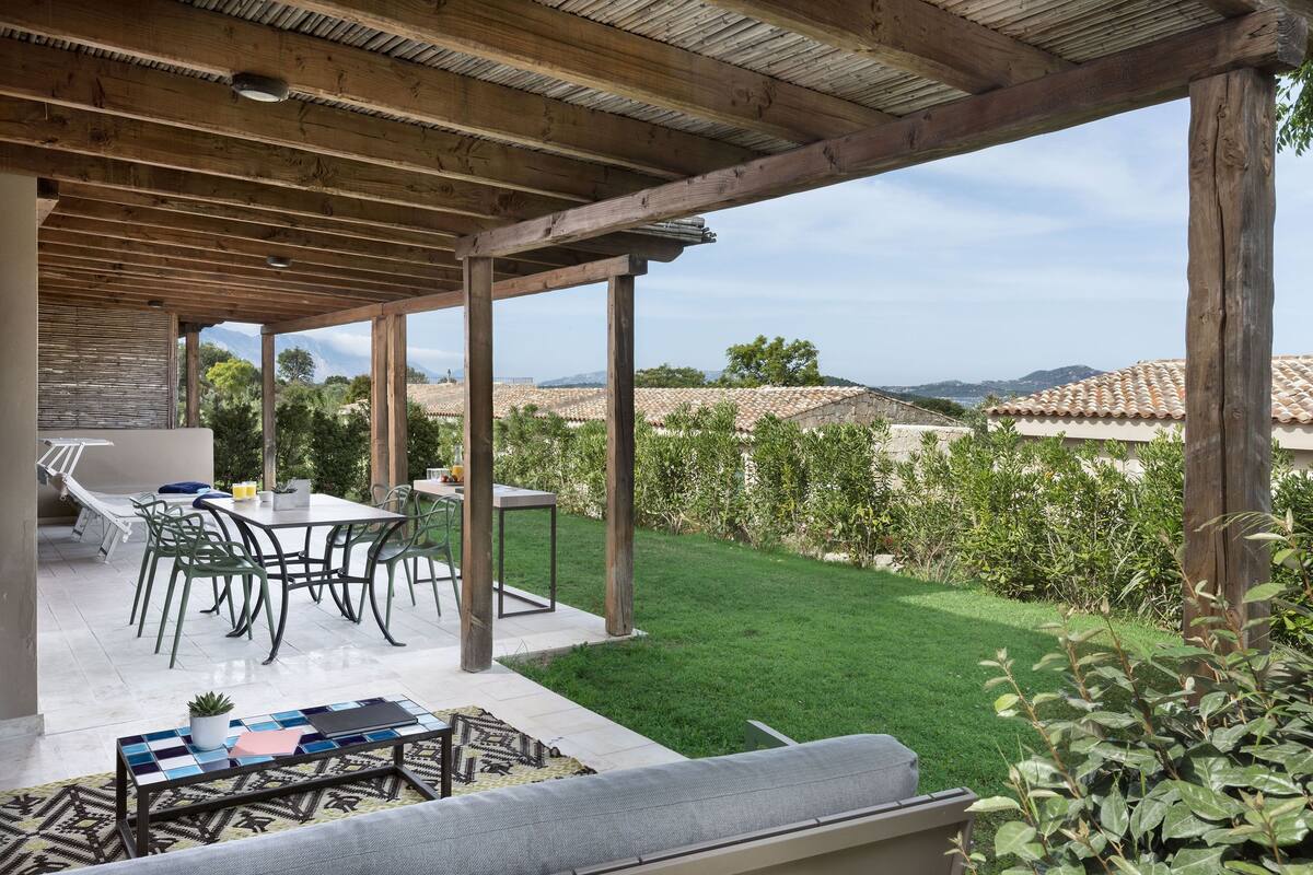 Une terrasse extérieure dotée d’une pergola en bois, d’une table à manger avec des chaises et offrant une vue sur le paysage environnant.