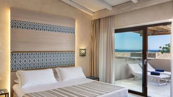 A hotel room with a bed, a nightstand, a patterned headboard, a large window with a view of the sea, and a balcony with a chair and table.