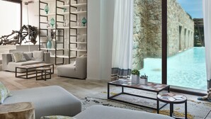 Una sala de estar moderna con un gran ventanal con vistas a una piscina, una estantería empotrada y un rincón de estar acogedor.