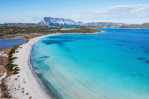 A coastal landscape with a beach, clear blue waters, and a mountain in the background. - Baglioni Resort Sardinia (San Teodoro)