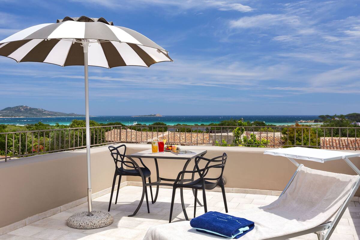 Un balcon avec une table, des chaises et un fauteuil, offrant une vue sur la côte.