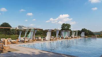Zona junto a la piscina con sillones de descanso y toldos, cielo despejado y montañas al fondo.