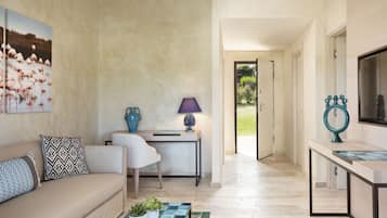 Un salon moderne avec un canapé beige, des coussins à motifs, une table basse agrémentée de plantes, une table d’appoint avec une lampe, et un tableau représentant des flamants roses accroché au mur.