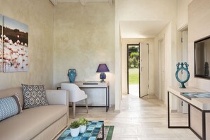 A modern living room with a beige sofa, patterned cushions, a coffee table with plants, a side table with a lamp, and a painting of flamingos on the wall. - Baglioni Resort Sardinia (San Teodoro)