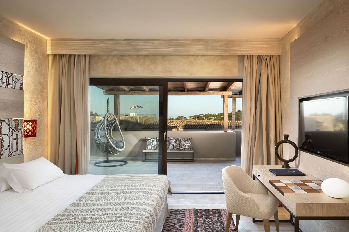 Une chambre d’hôtel moderne, dotée d’un grand lit, d’un bureau avec une chaise, d’une télévision et offrant une vue sur le paysage urbain.