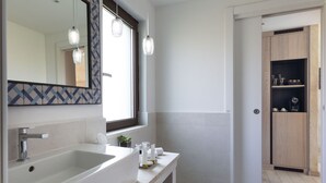 A modern bathroom with a large mirror, two pendant lights, a white sink, and a wooden cabinet.