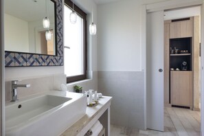 A modern bathroom with a large mirror, two pendant lights, a white sink, and a wooden cabinet. - Baglioni Resort Sardinia (San Teodoro)