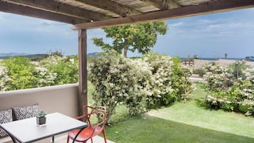 A covered patio with a table and chairs, a view of a landscaped garden with flowering bushes, and a distant landscape.